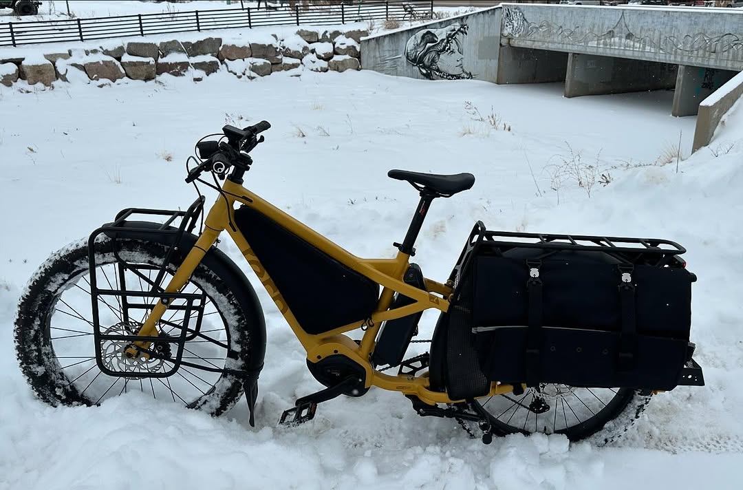 A yellow longtail cargo bike parked in the snow